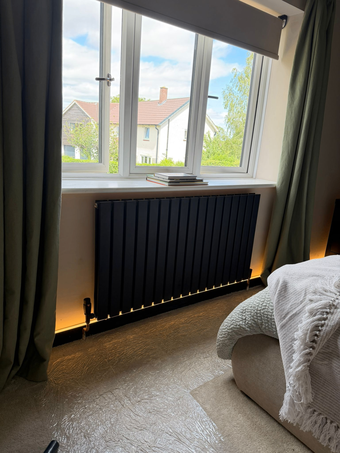 Matte black vertical flat-panel designer radiator installed under bedroom window during heating upgrade
